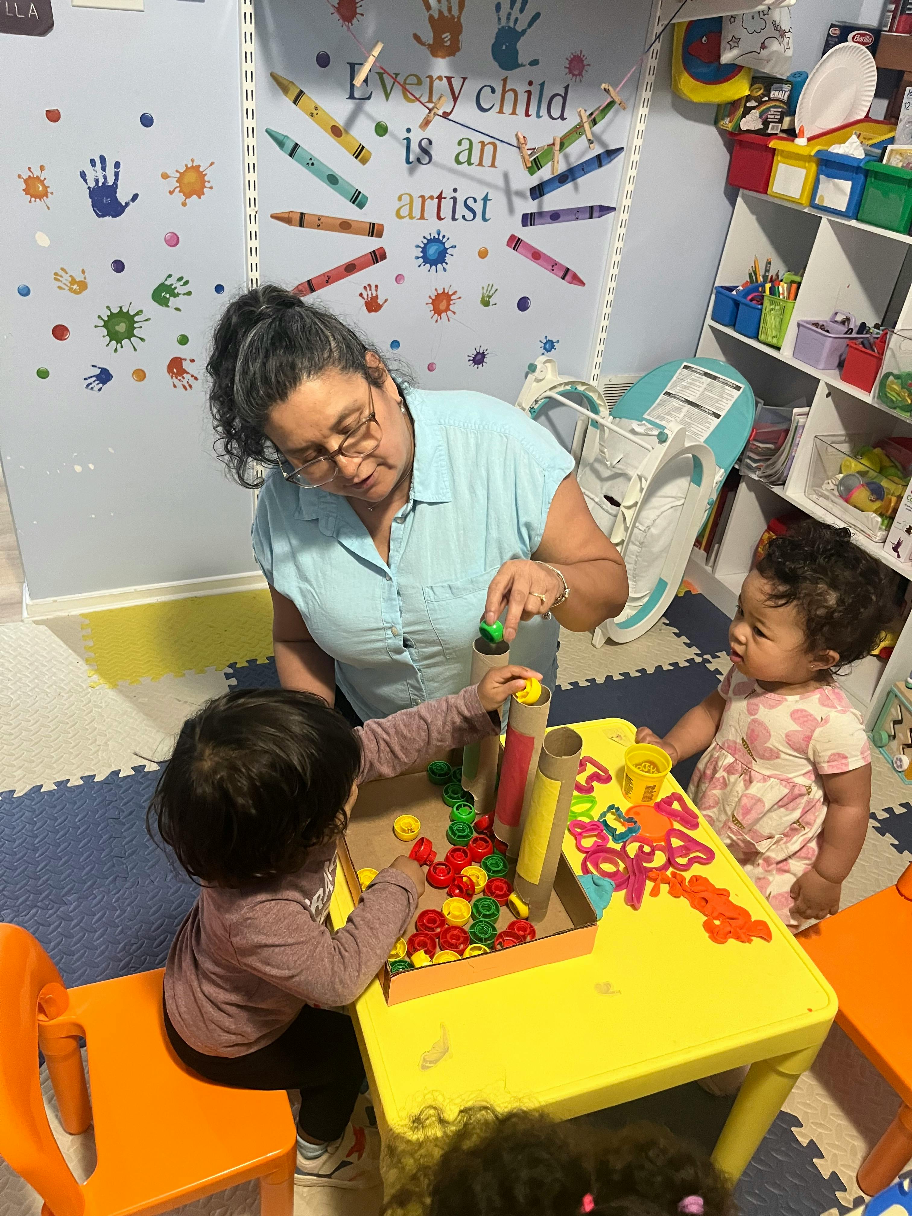 Adult and two children playing with colorful shapes and tubes at a table