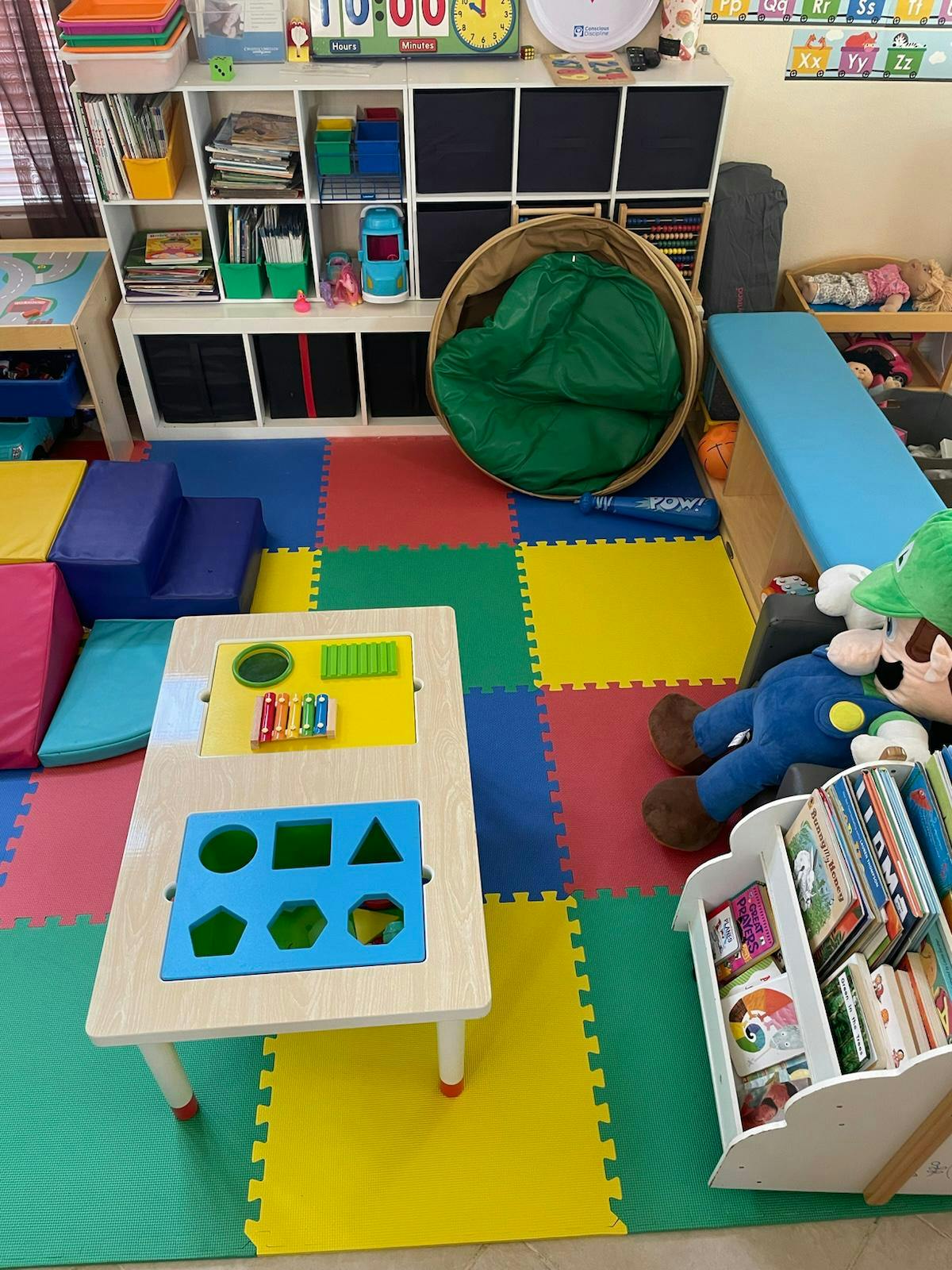 Playroom with colorful floor mats, a small table, and shelves with toys and shelves