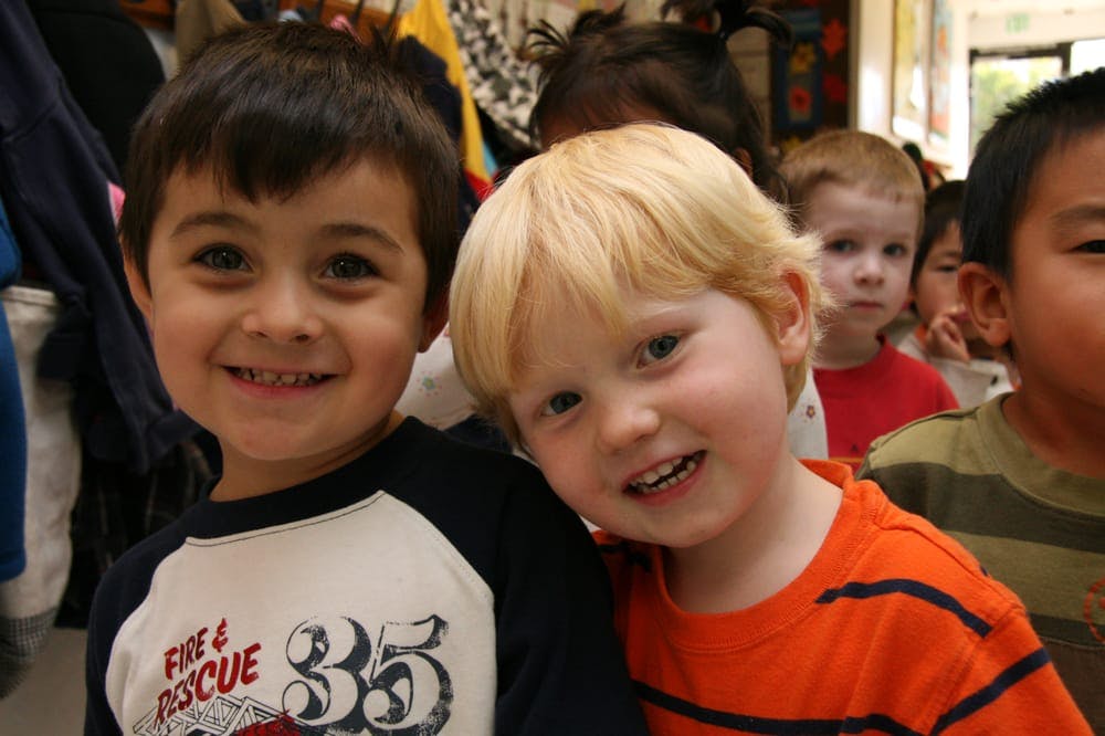 Two children smiling at the camera, with other children in the background