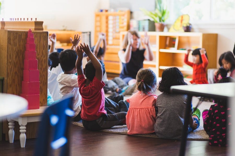 Children sitting on the floor with hands raised in a classroom