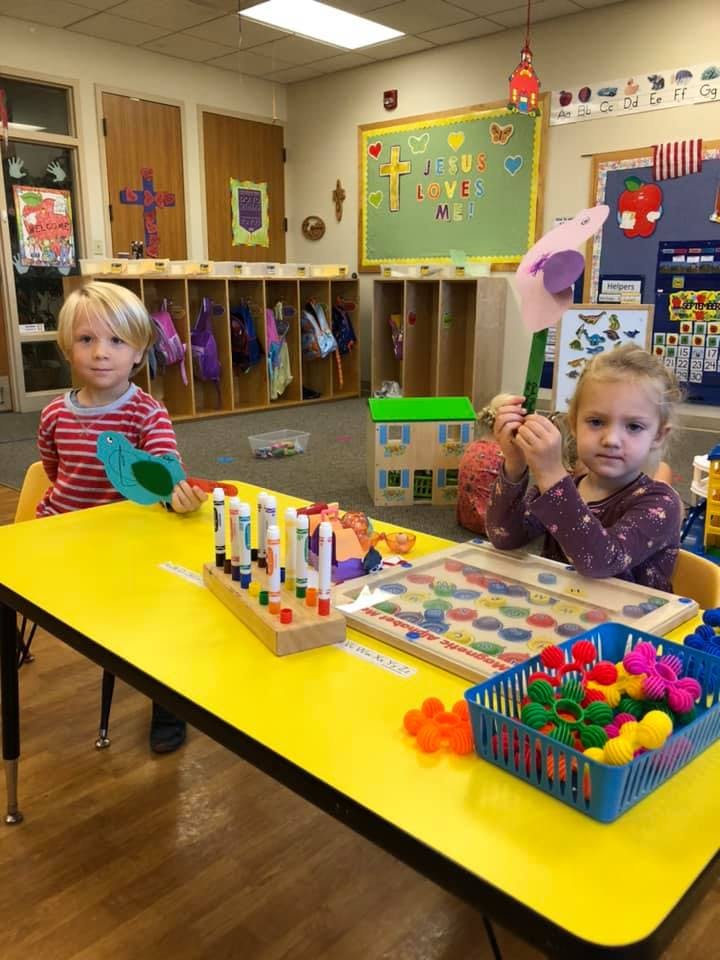 Two children at a yellow table with toys in a classroom