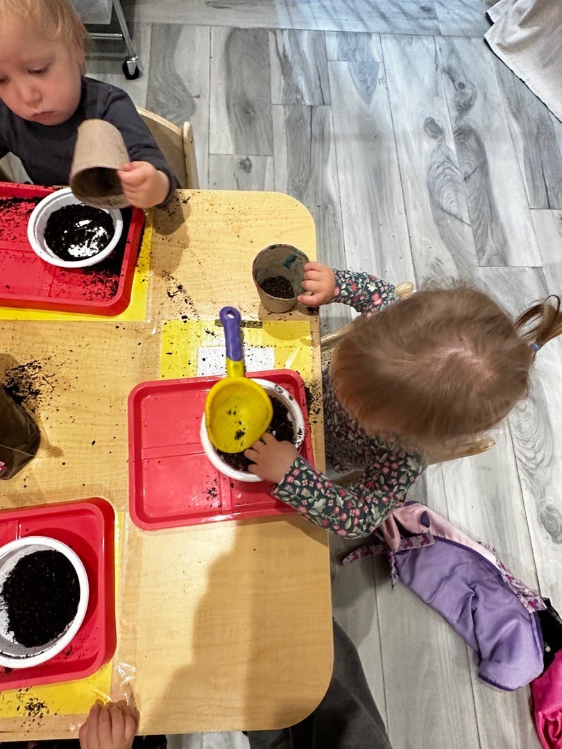 Two children playing with soil and small pots at a table