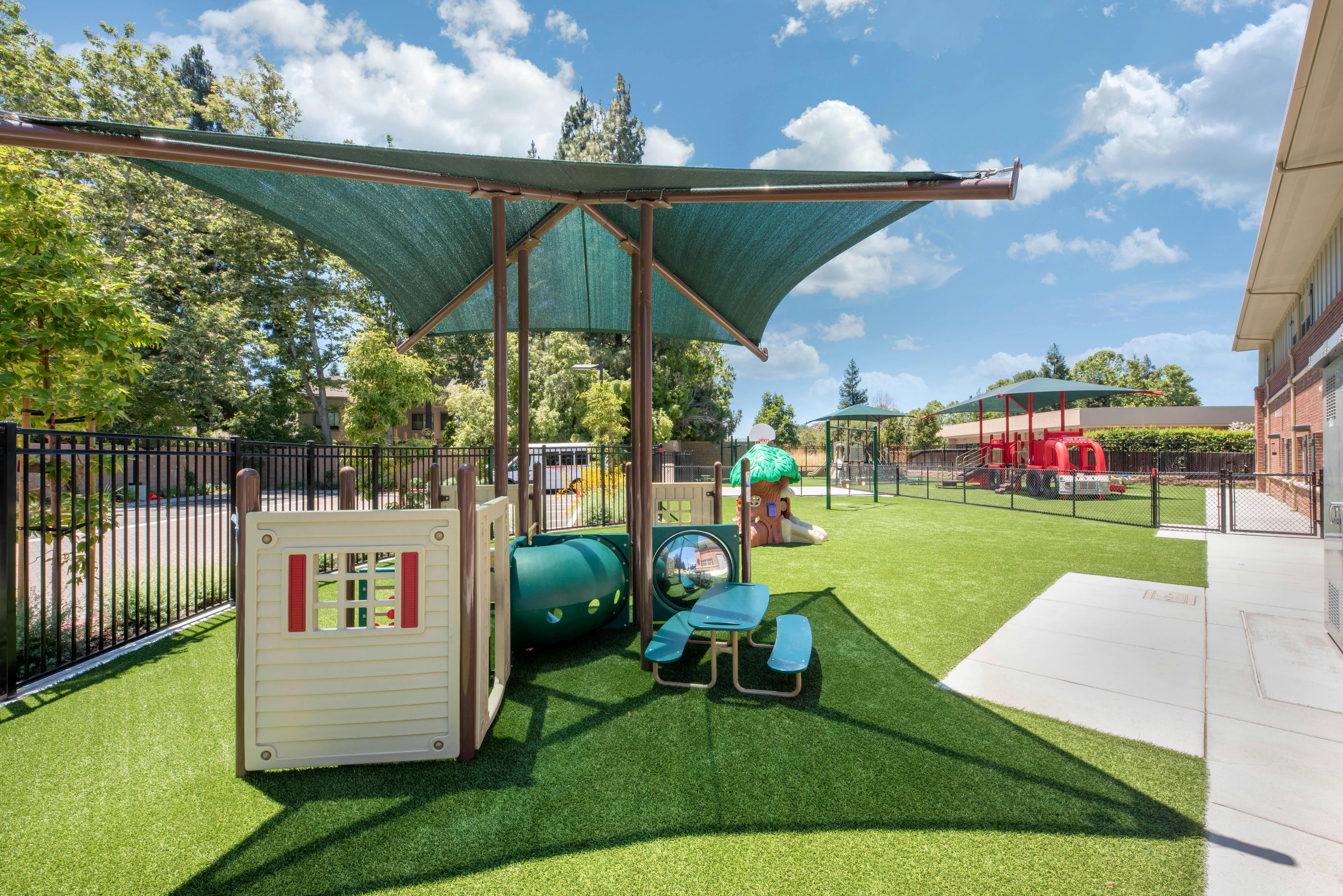 Outdoor children's playground with artificial turf, play structures, and shade covering