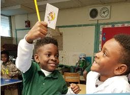 Child holding up a card on a stick to another child in a classroom