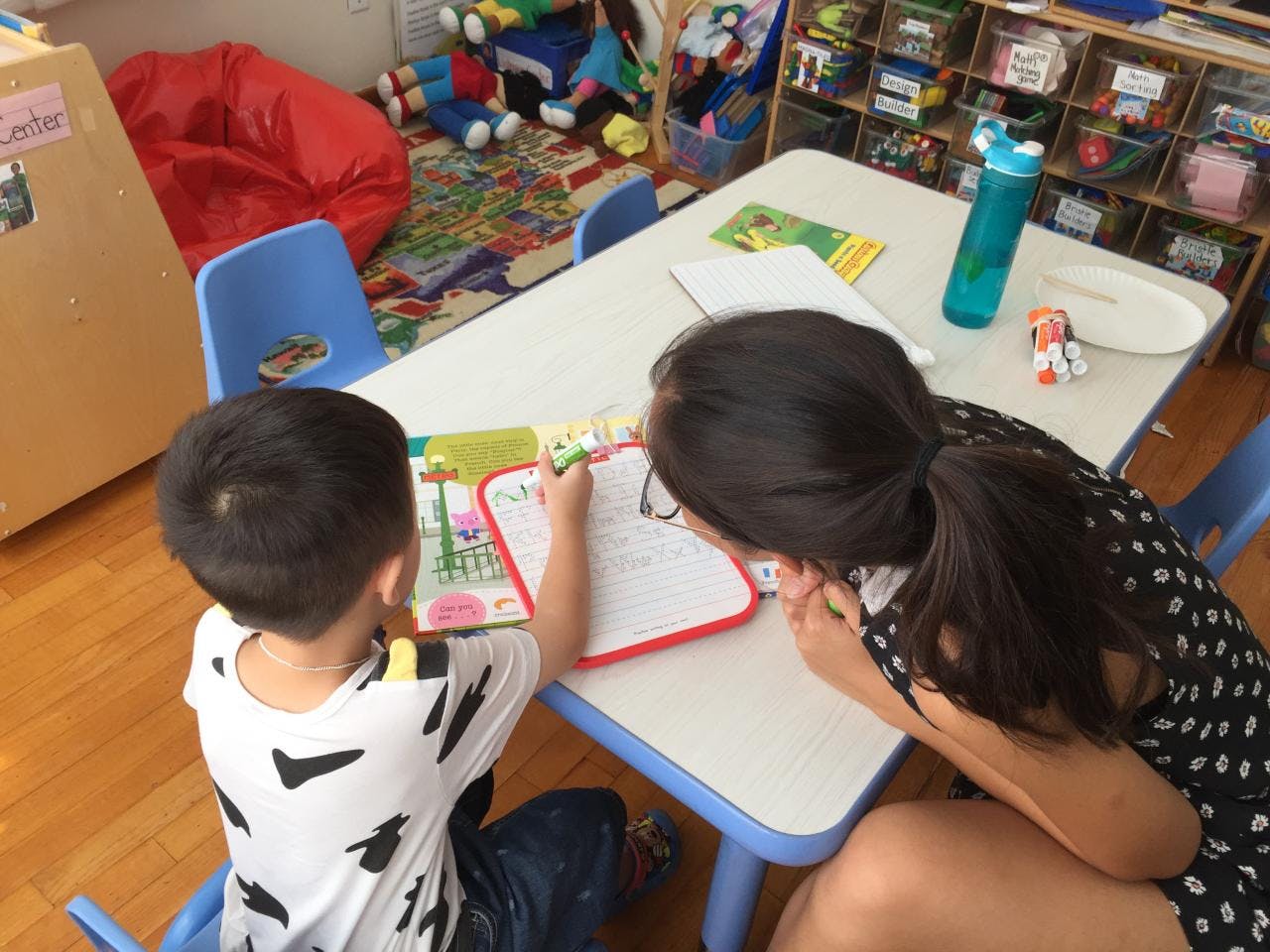 Adult and child drawing on a whiteboard at a table in a classroom