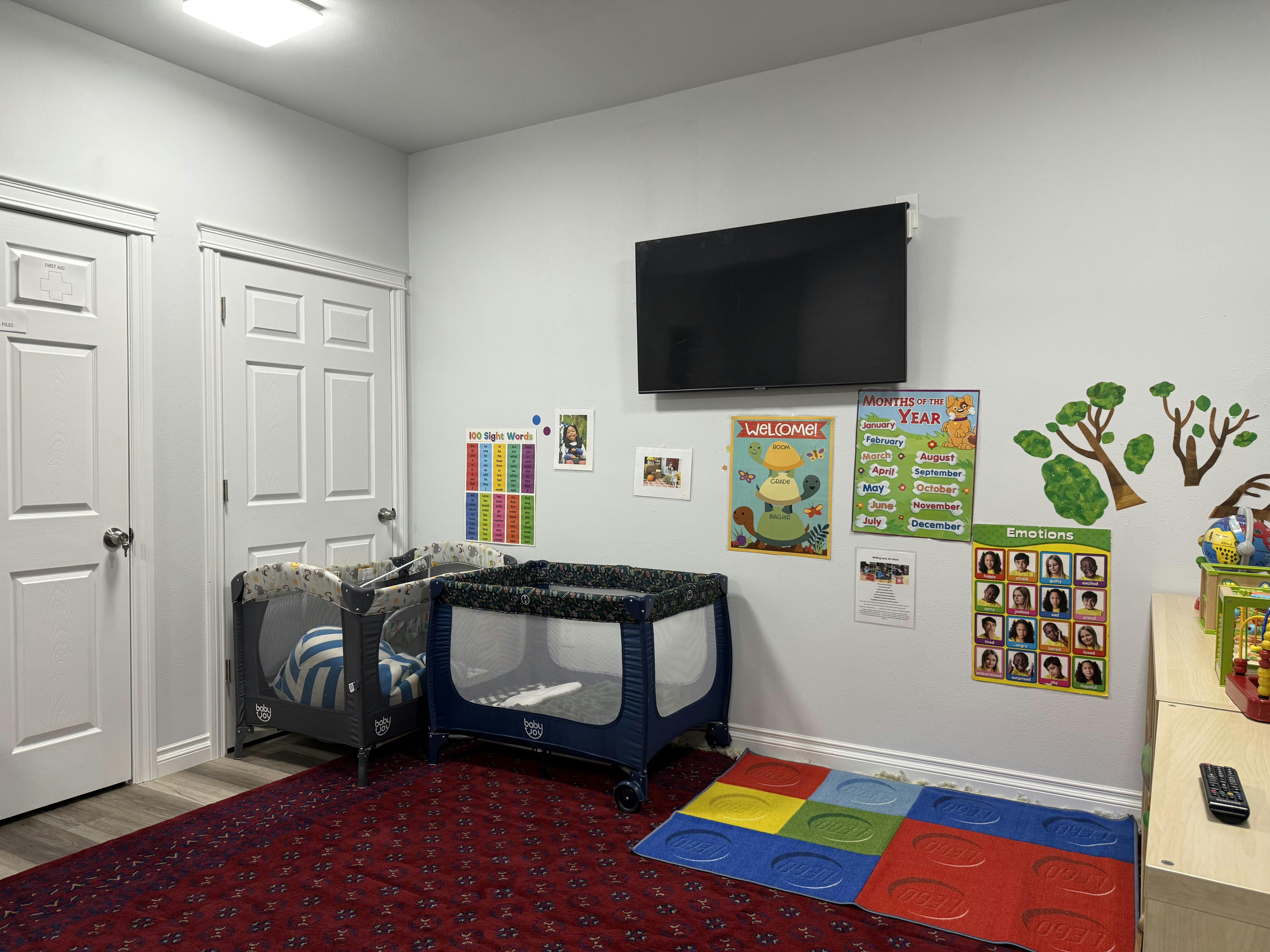A room with two playpens, a TV, and educational posters on the wall