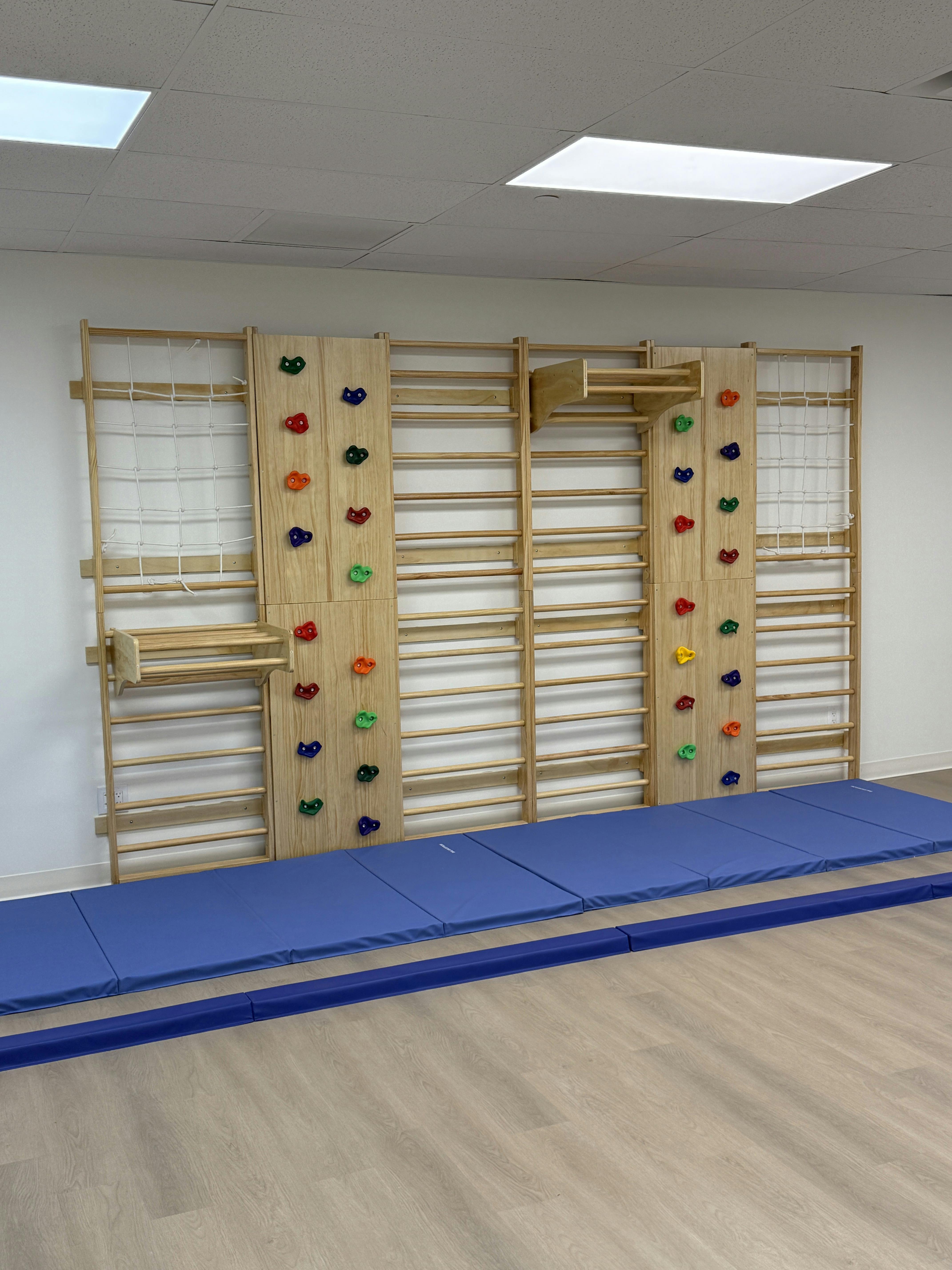Wooden climbing wall with colorful holds and blue mats on the floor