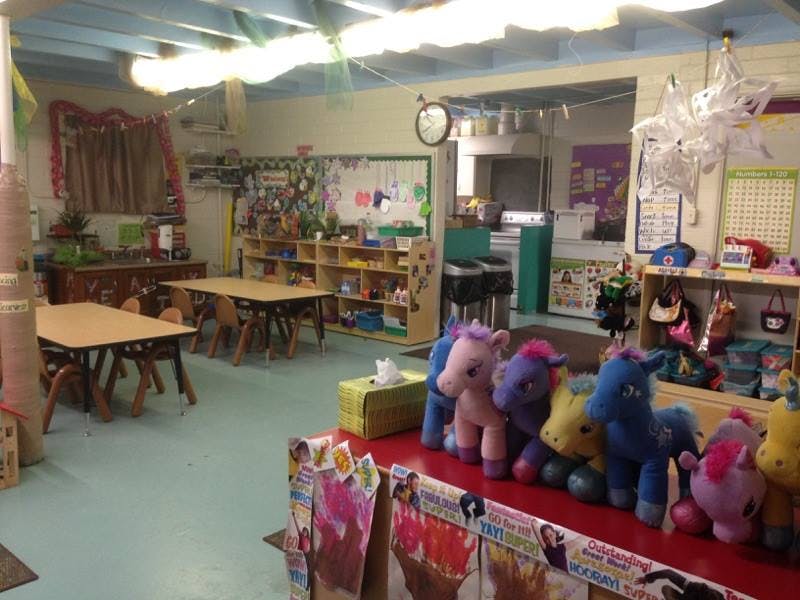 Classroom with small tables and chairs, shelves with toys, and stuffed animals