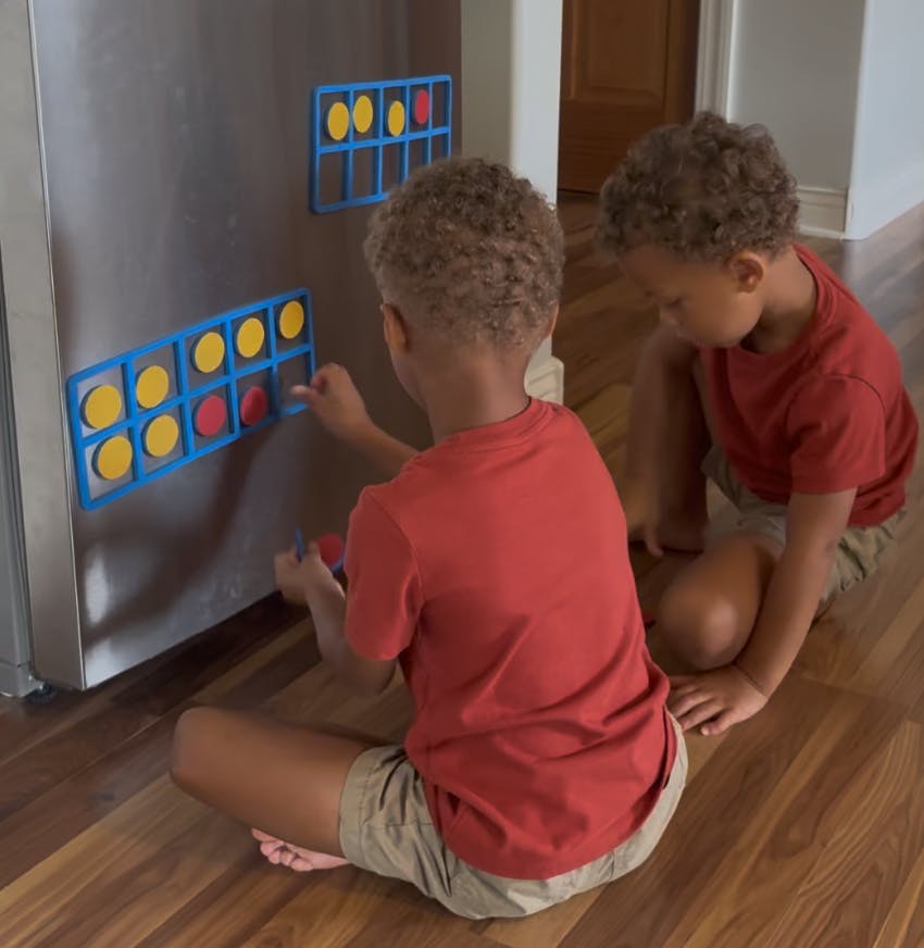 Two children sitting on a floor placing magnetic circles on a ten-frame chart