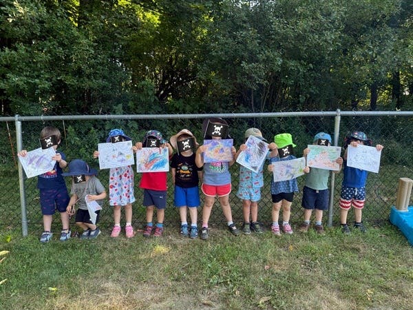 Group of children holding up drawings in front of a fence
