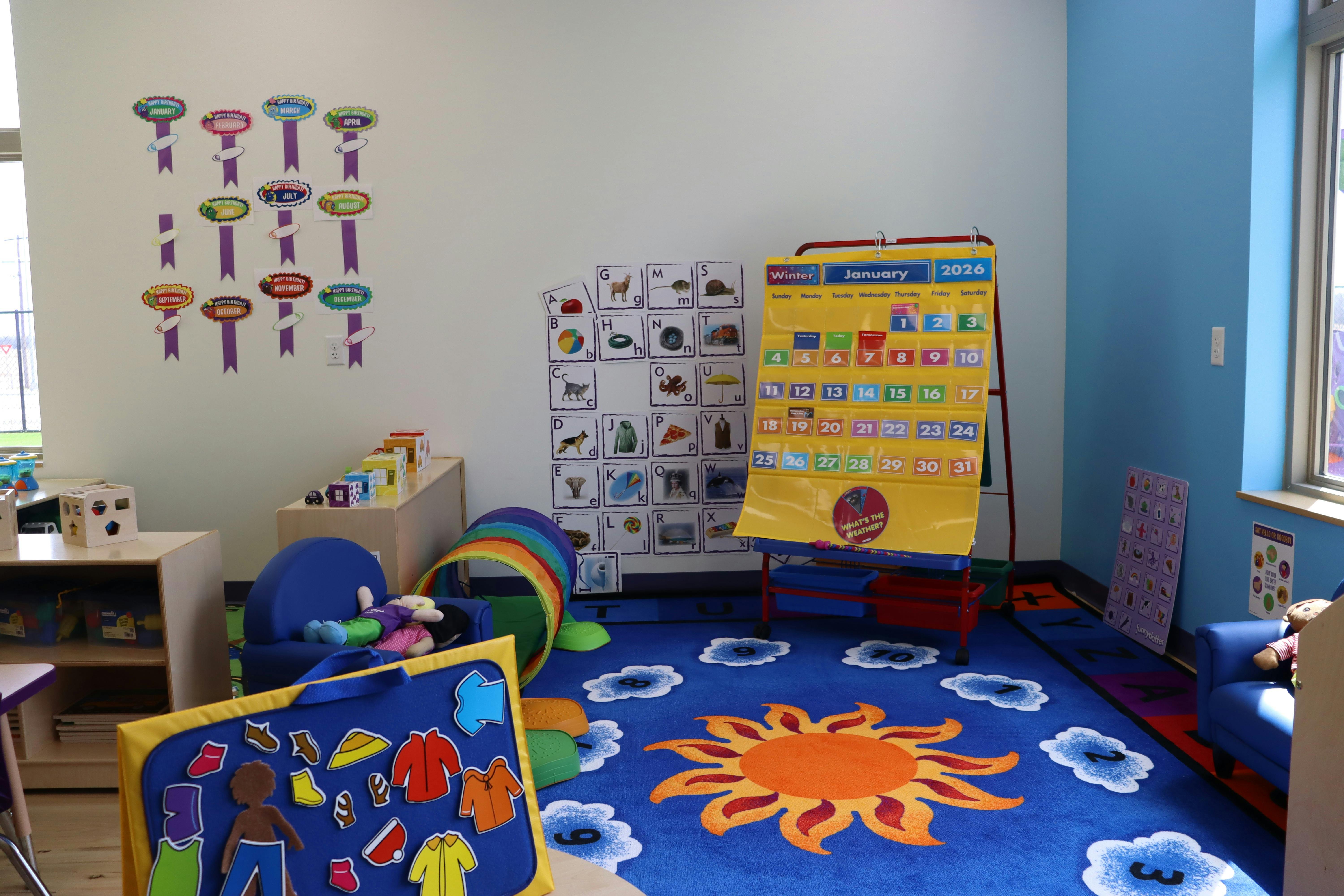 Classroom with calendar, alphabet chart, birthday chart, rainbow tunnel, and rug