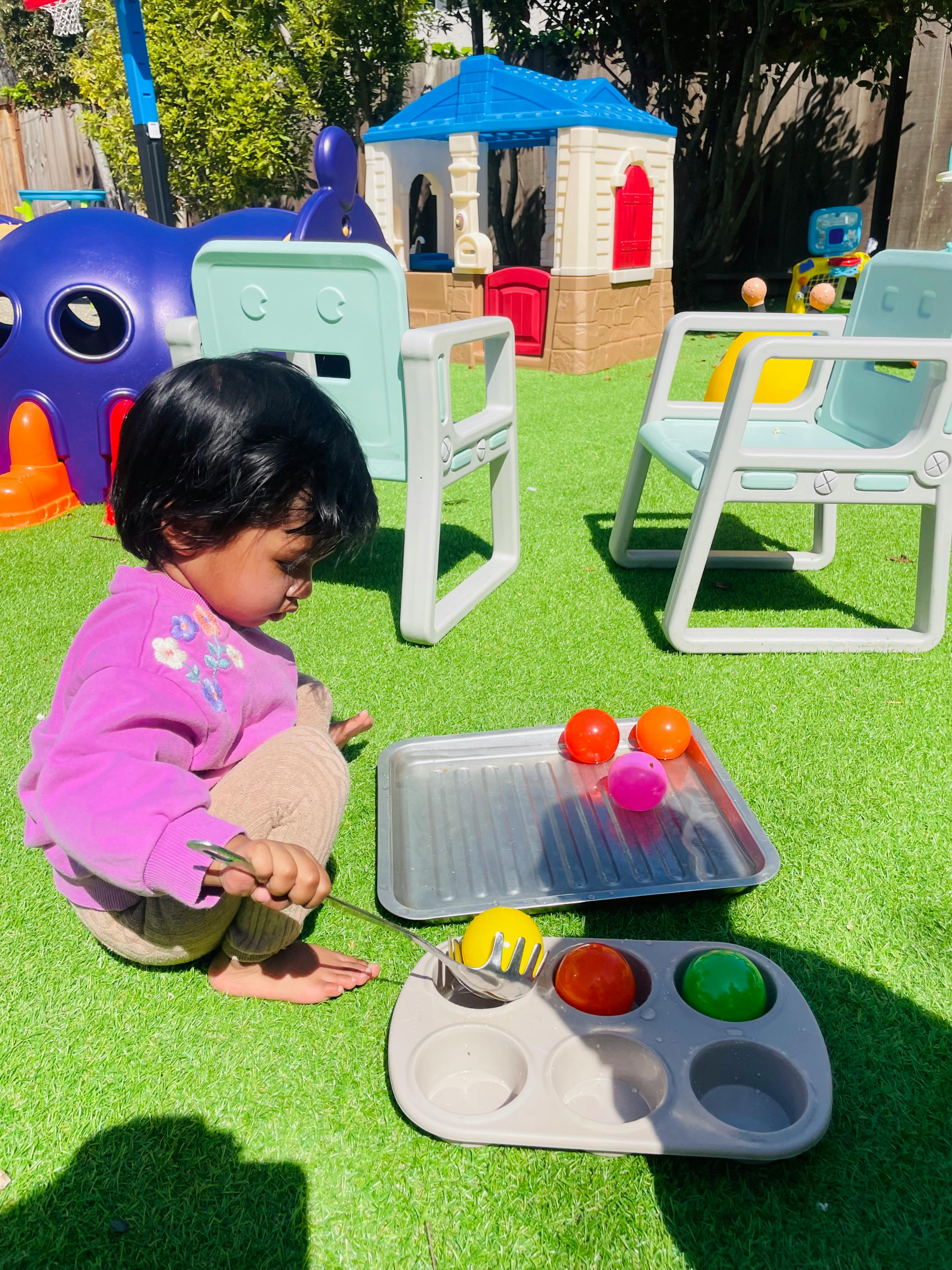 Child playing with colorful balls and kitchen utensils on artificial grass