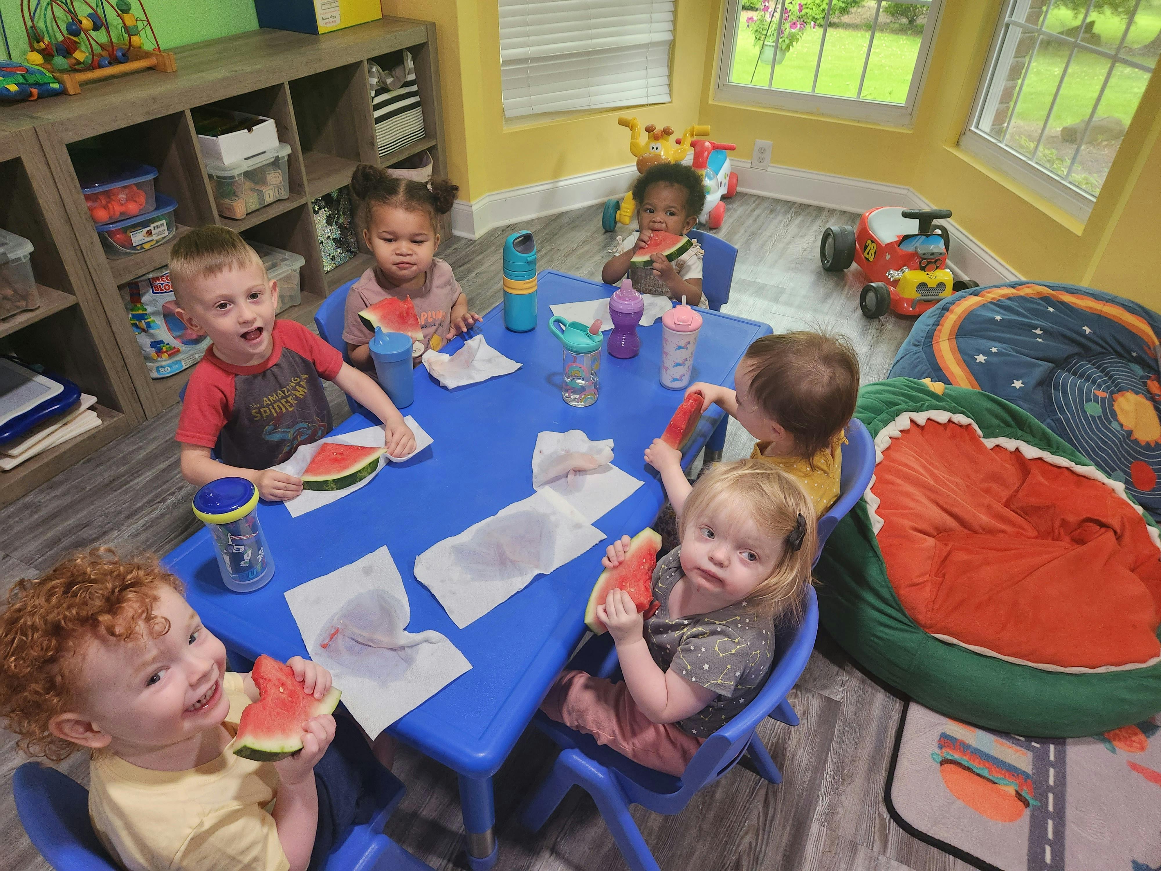 Children eating watermelon at a blue table