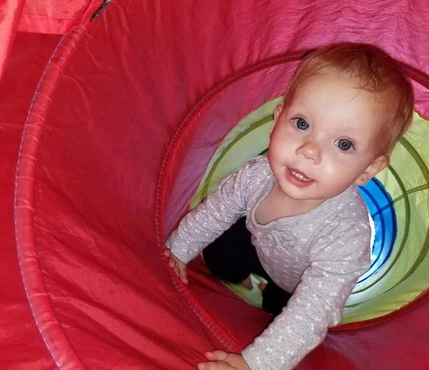 Child crawling through a red and green play tunnel