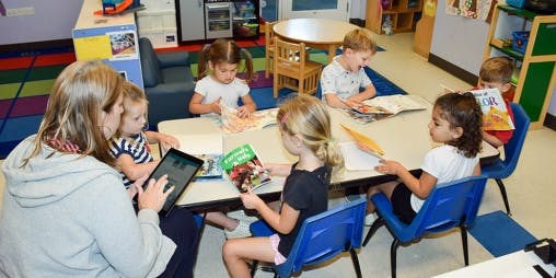 Person and children reading books and using a tablet in a classroom