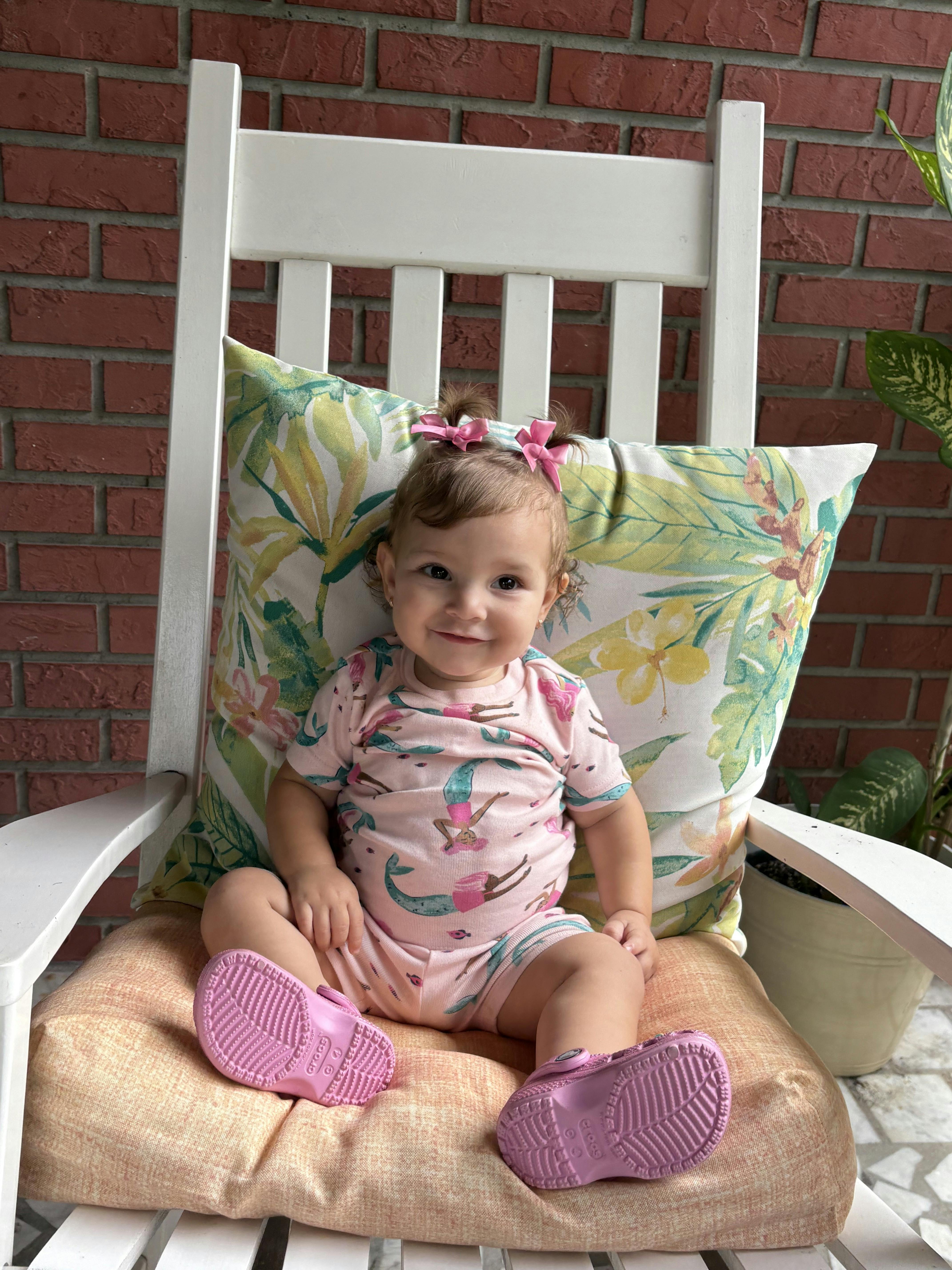 Child sitting on a white rocking chair with a patterned pillow
