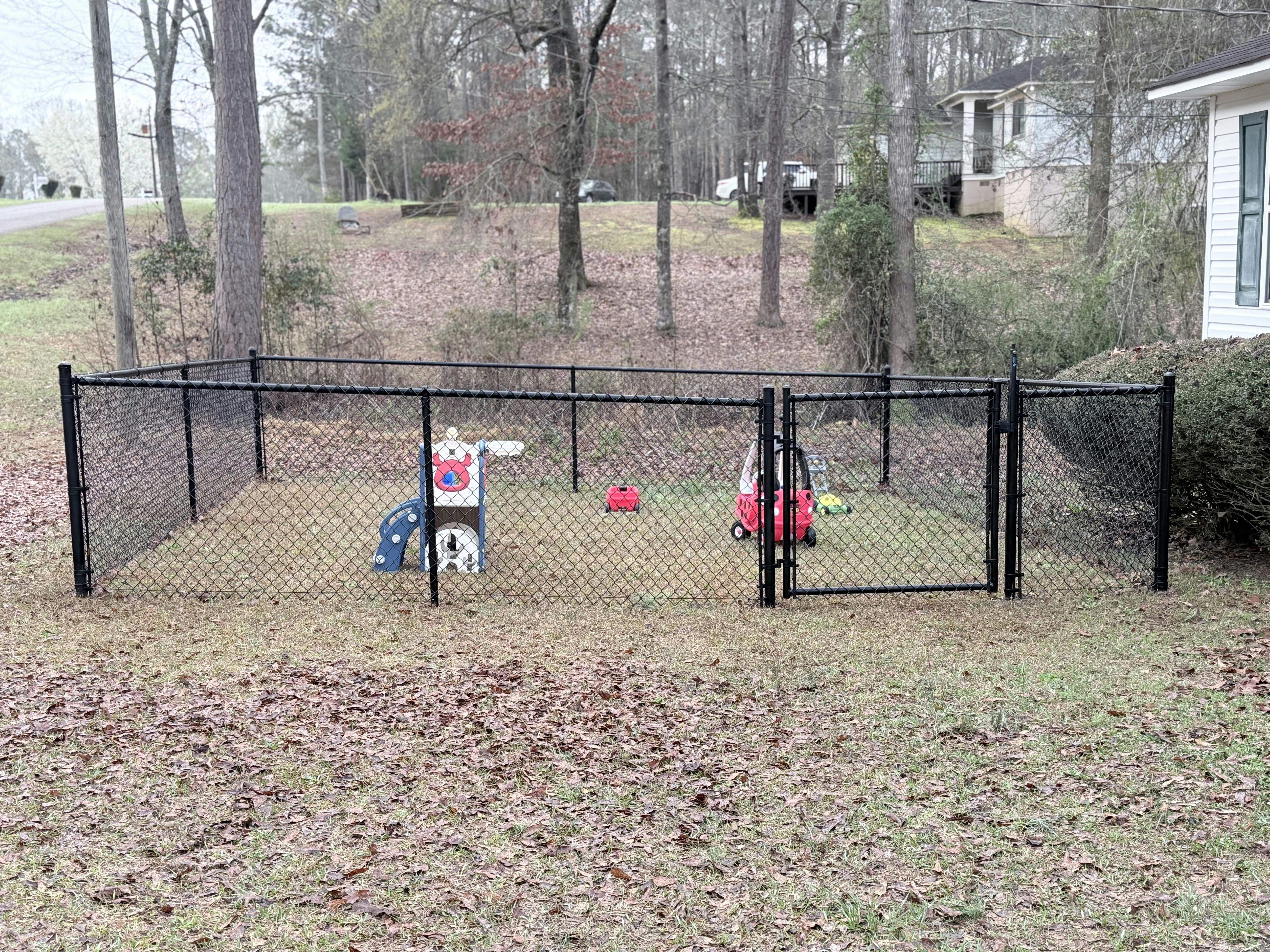 Black chain-link fence enclosing a playground area with toys on grass
