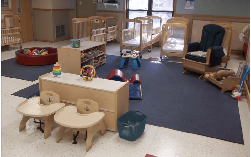 A childcare classroom with cribs, high chairs, and various toys