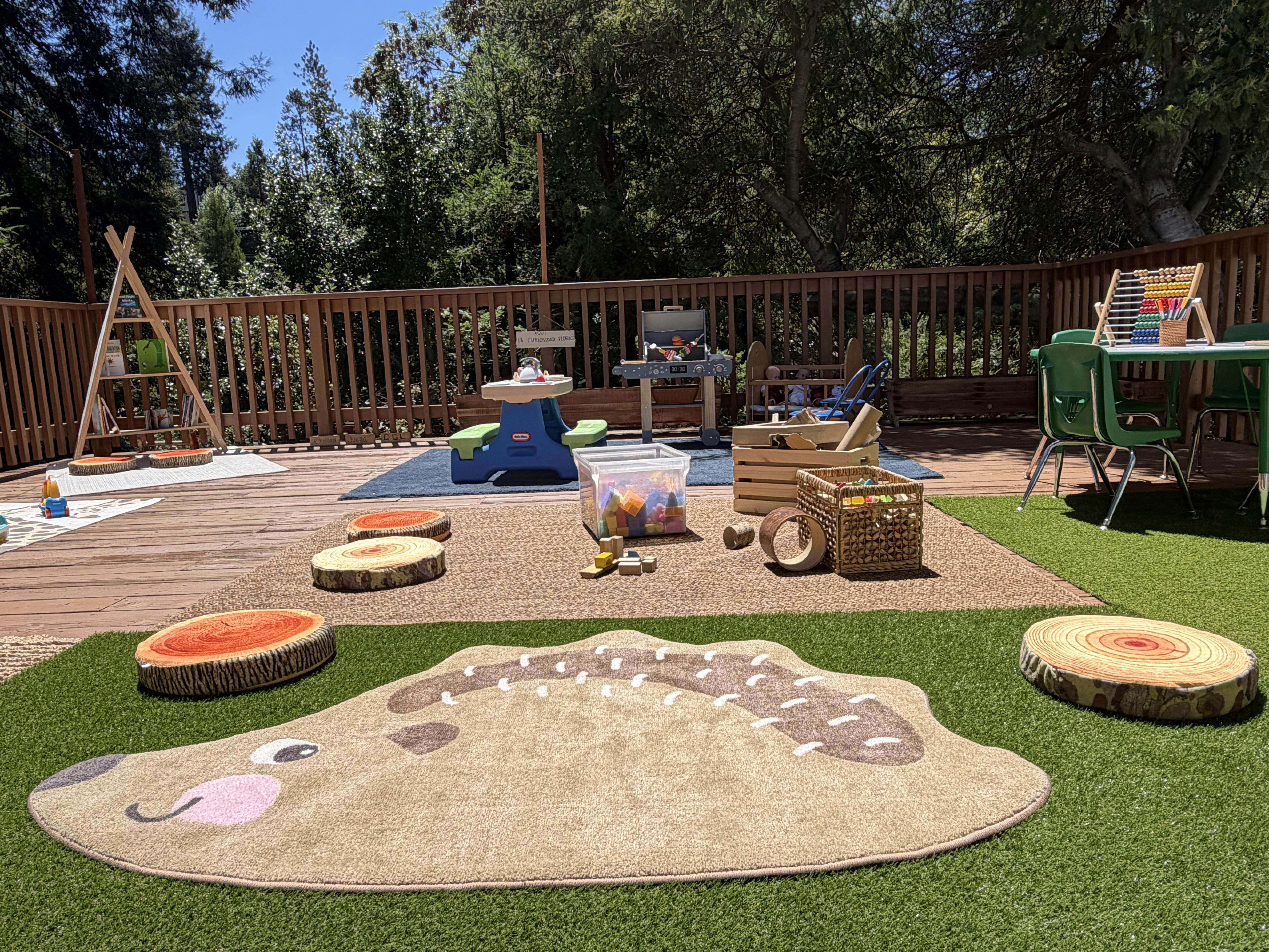 Outdoor children play area with rugs, wooden log cushions, and various toys