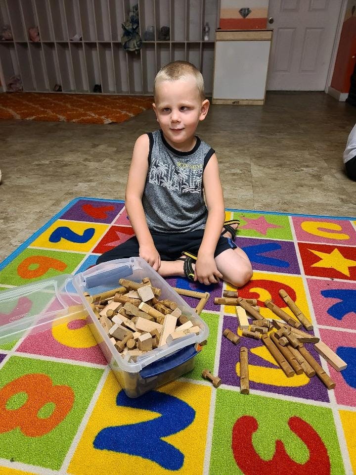 Child sitting on a colorful rug with a container of wooden blocks