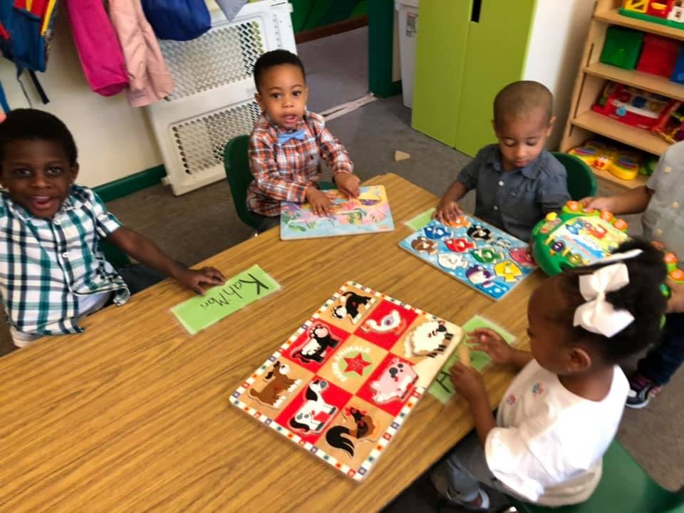 Four children playing with puzzles at a table in a classroom