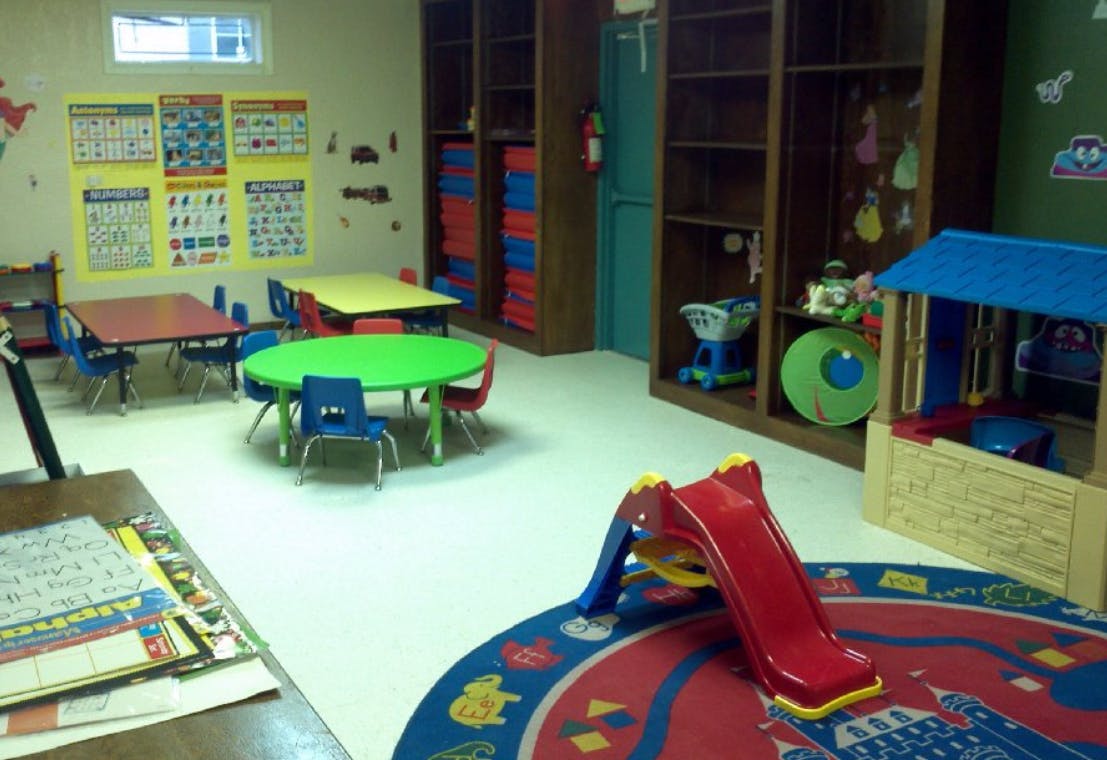 Playroom with small tables and chairs, a slide, and shelves with shelves of toys