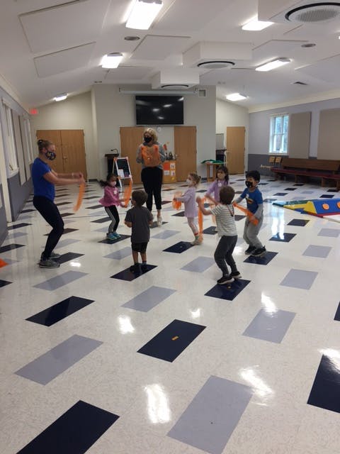 Adults and children in a room with patterned floor, holding orange objects