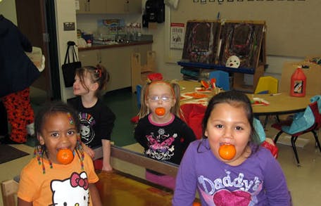 Children with oranges in their mouths in a classroom