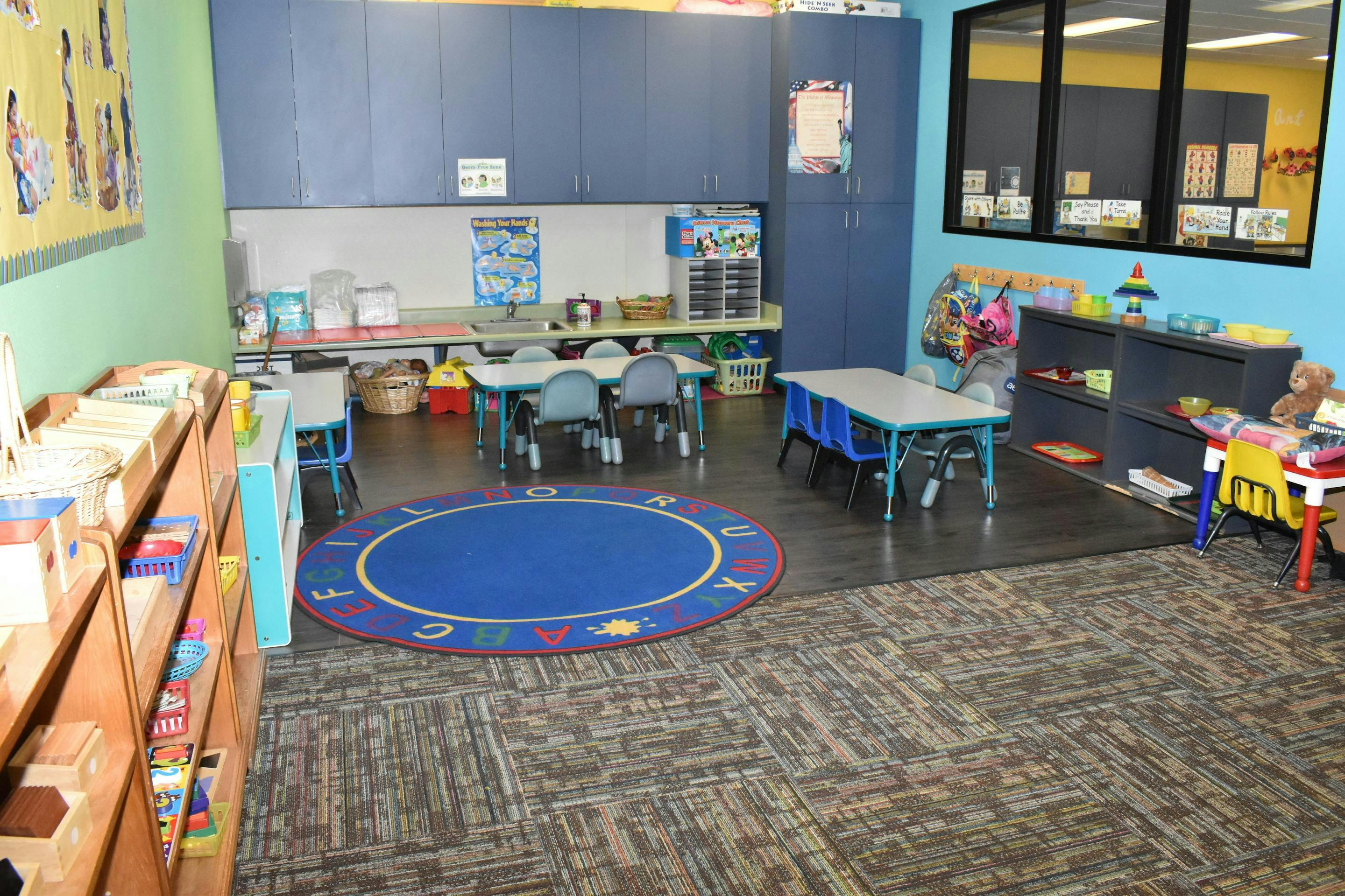 Classroom with small tables and chairs, a blue circular rug, and shelves