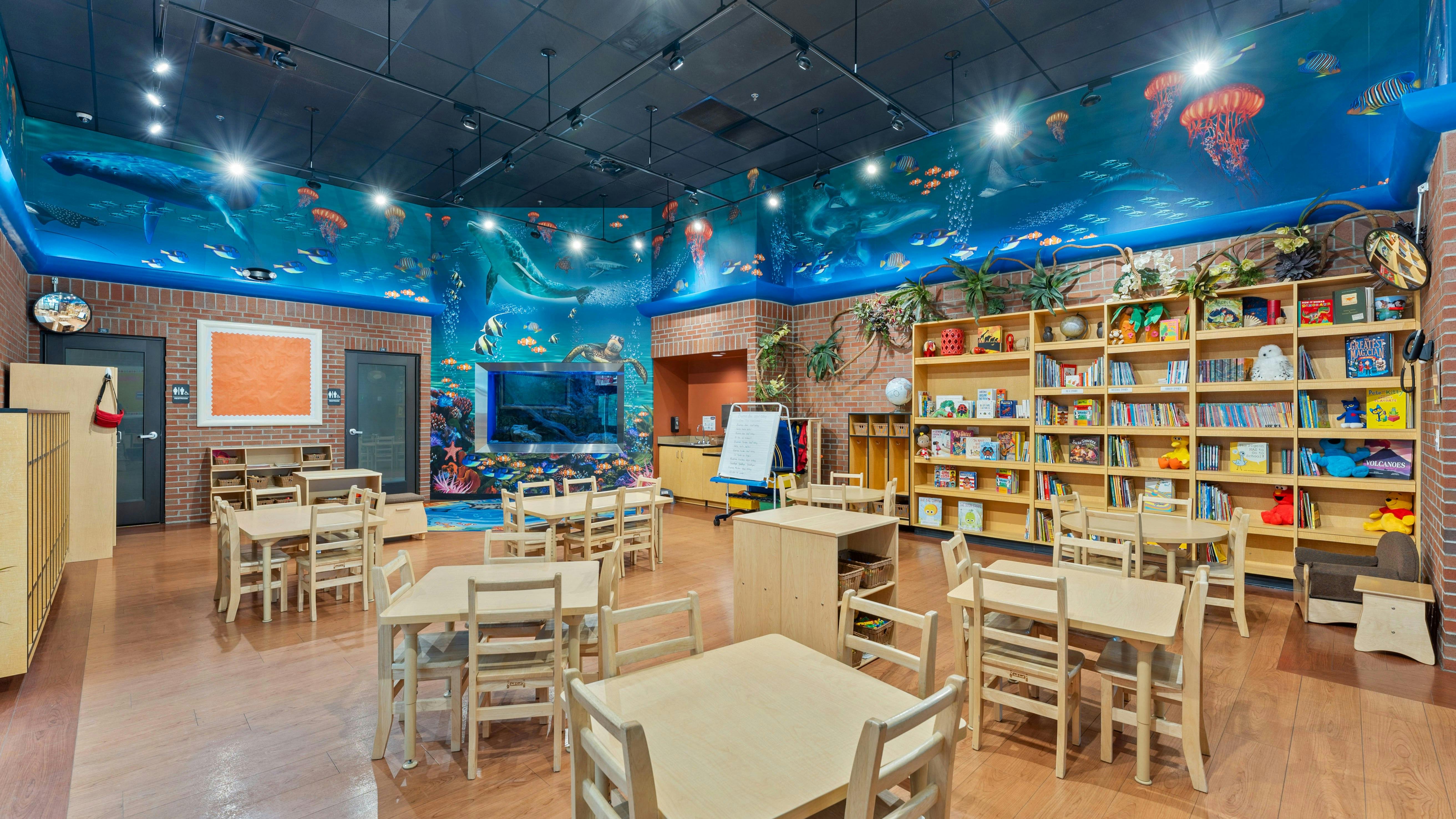 Classroom with ocean-themed wall murals, tables, chairs, and bookshelves