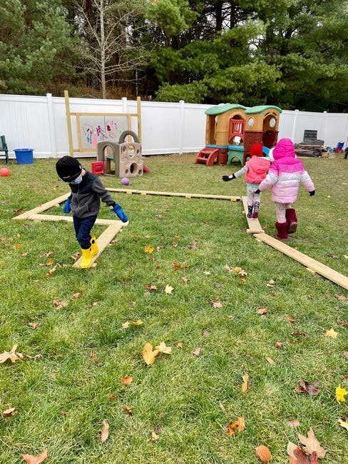 Children walking on wooden planks in a grassy outdoor play area