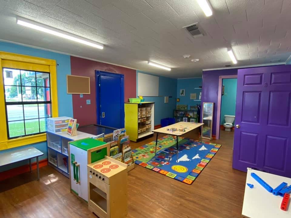 Playroom with colorful walls, play kitchen, tables, and rugs