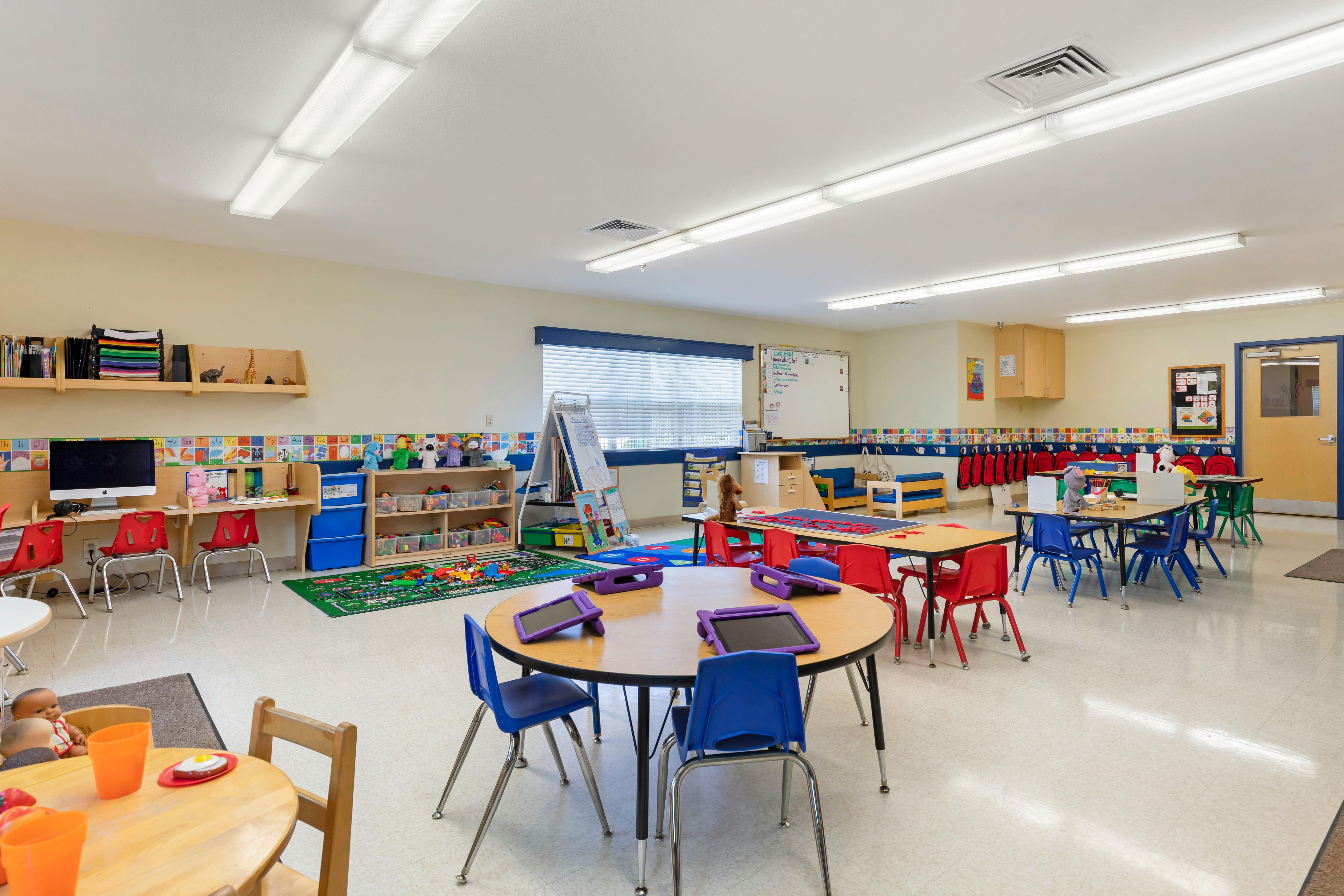 A colorful empty classroom with small tables, chairs, and learning materials