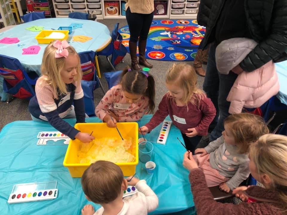 Children gathered around a table with a yellow bin of sensory materials