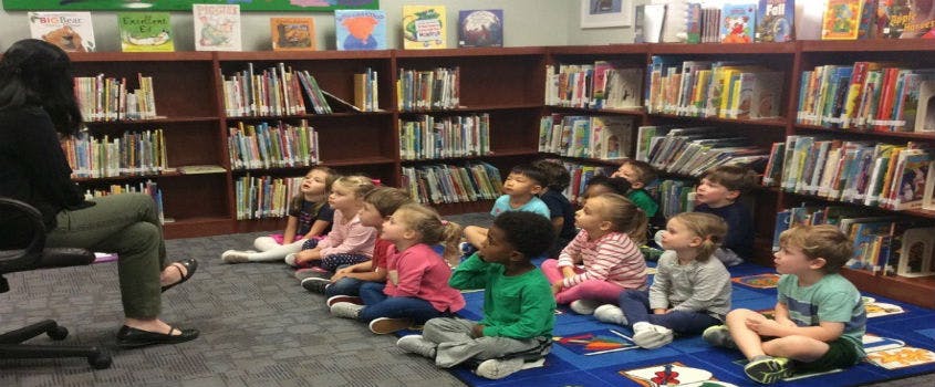 Person sitting in a chair reading to children sitting on the floor in a library