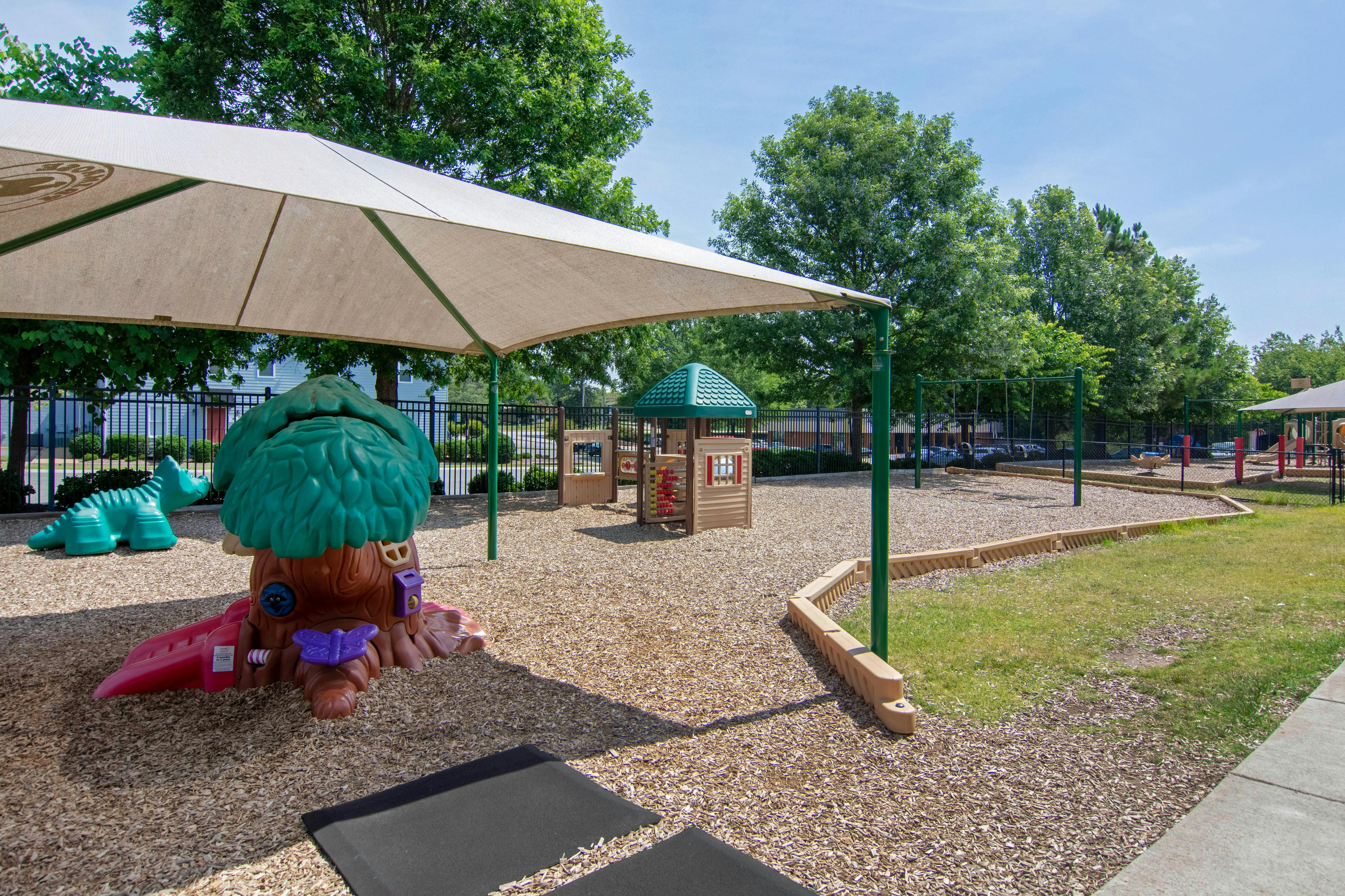 Playground area with shade canopy, small treehouse slide, and dinosaur toy