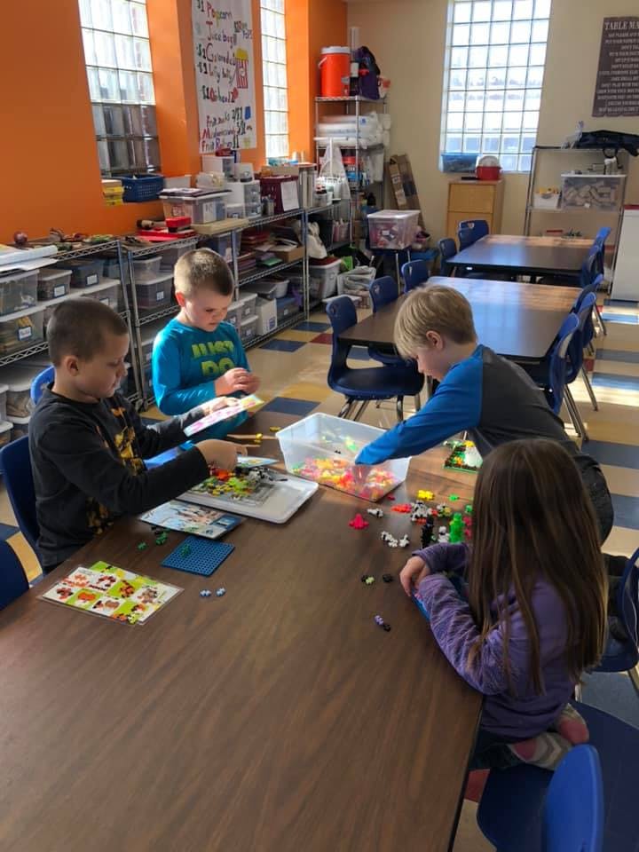 Four children playing with building blocks at a table in a classroom