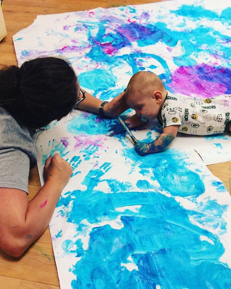 Person and child painting on a large sheet of paper on the floor
