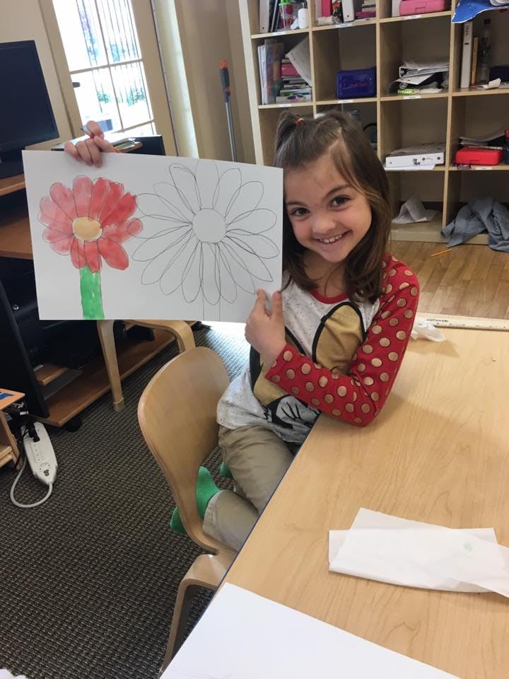 Child holding up a drawing of a flower, partially colored