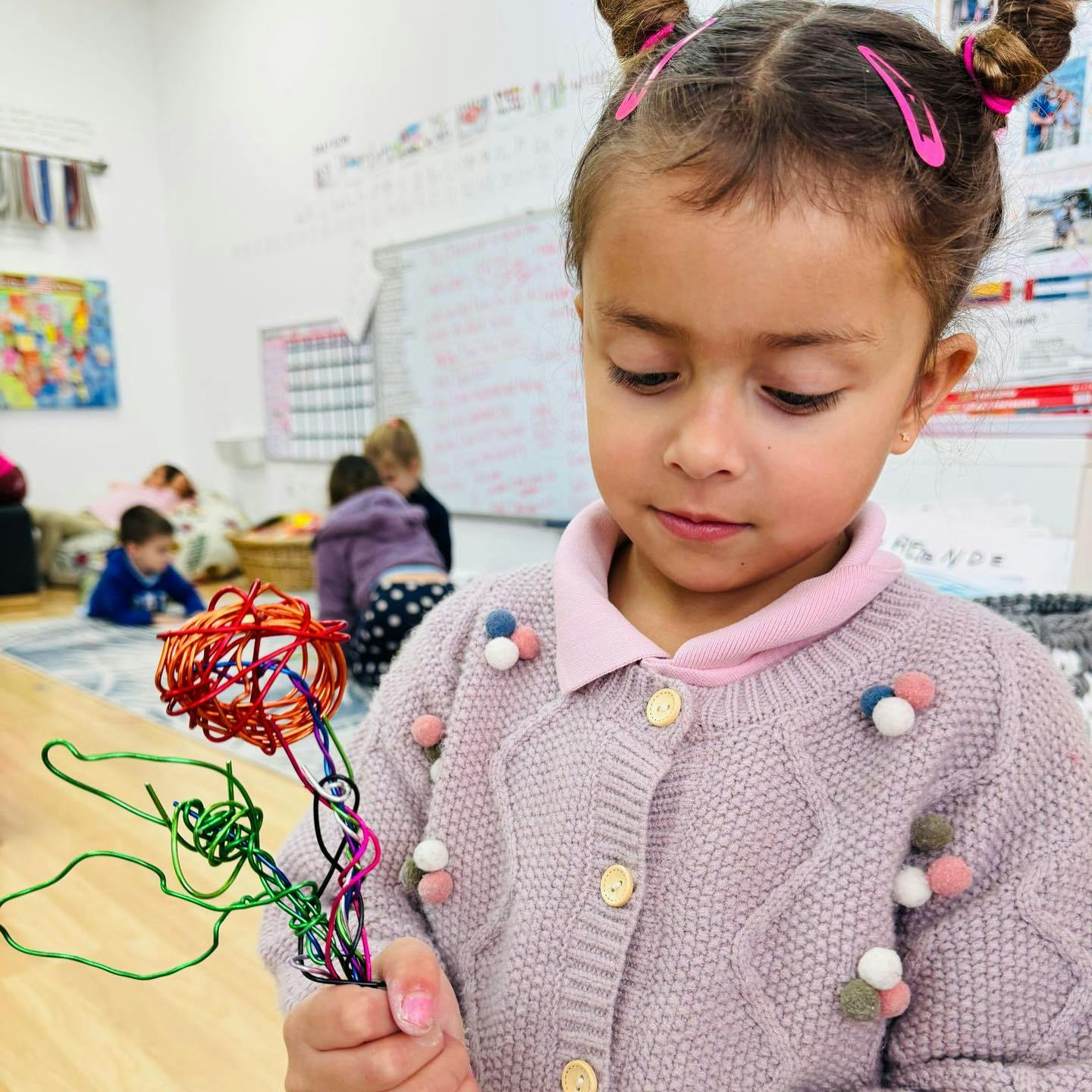 Child holding a colorful wire sculpture in a classroom