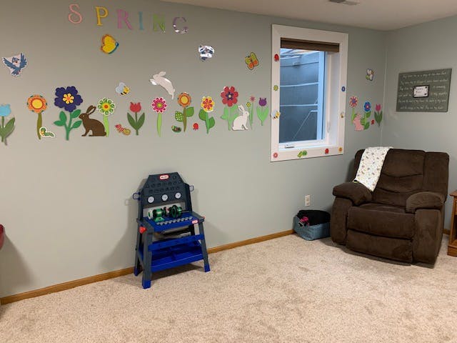 Wall decorated with colorful flower and animal cutouts, a window, and a recliner