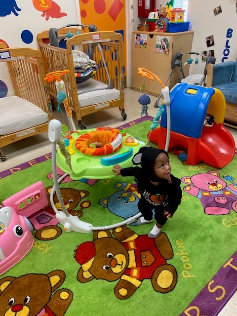 Child in a black outfit standing on a green rug with teddy bears