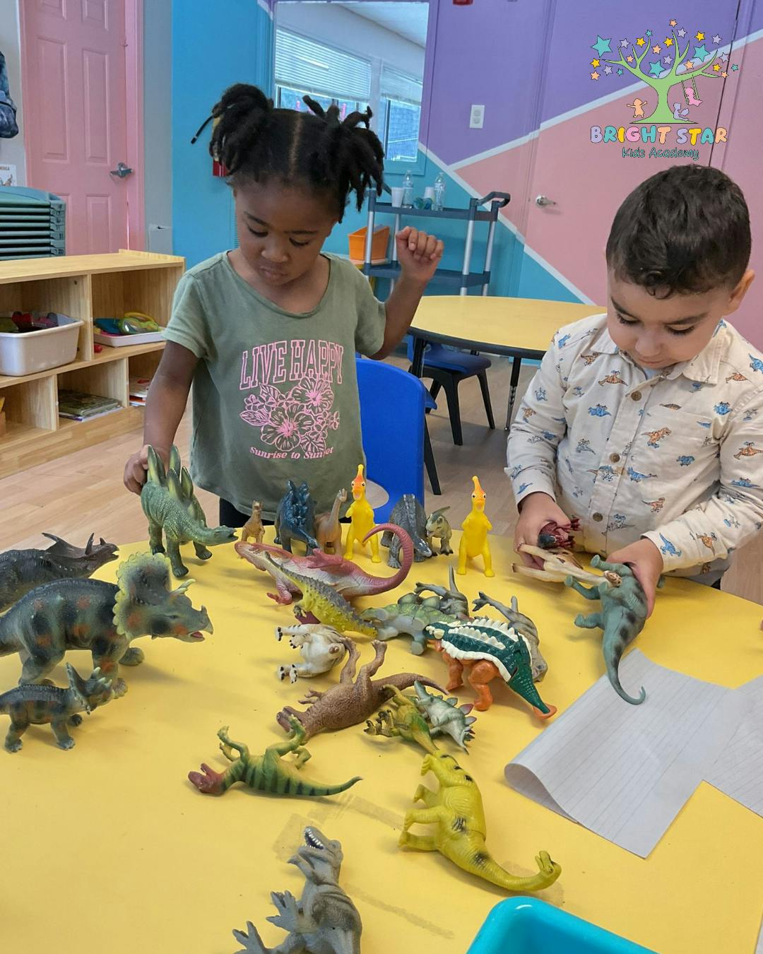 Two children playing with dinosaur toys on a yellow table