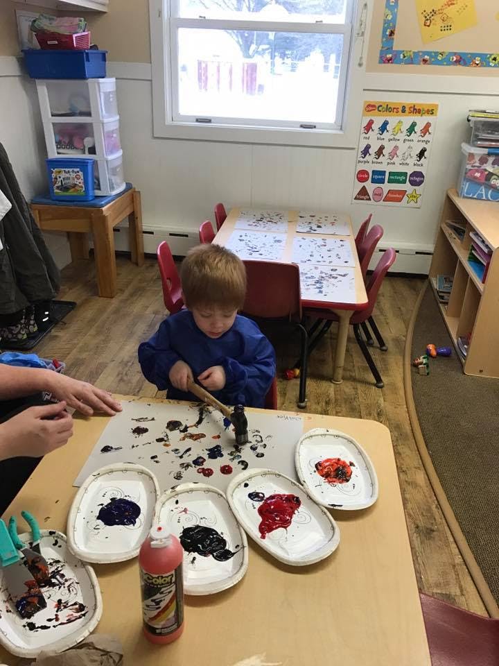 Child painting with a hammer in a classroom