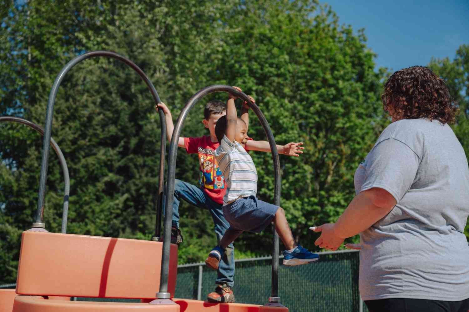 Two children playing on playground equipment, with an adult observing
