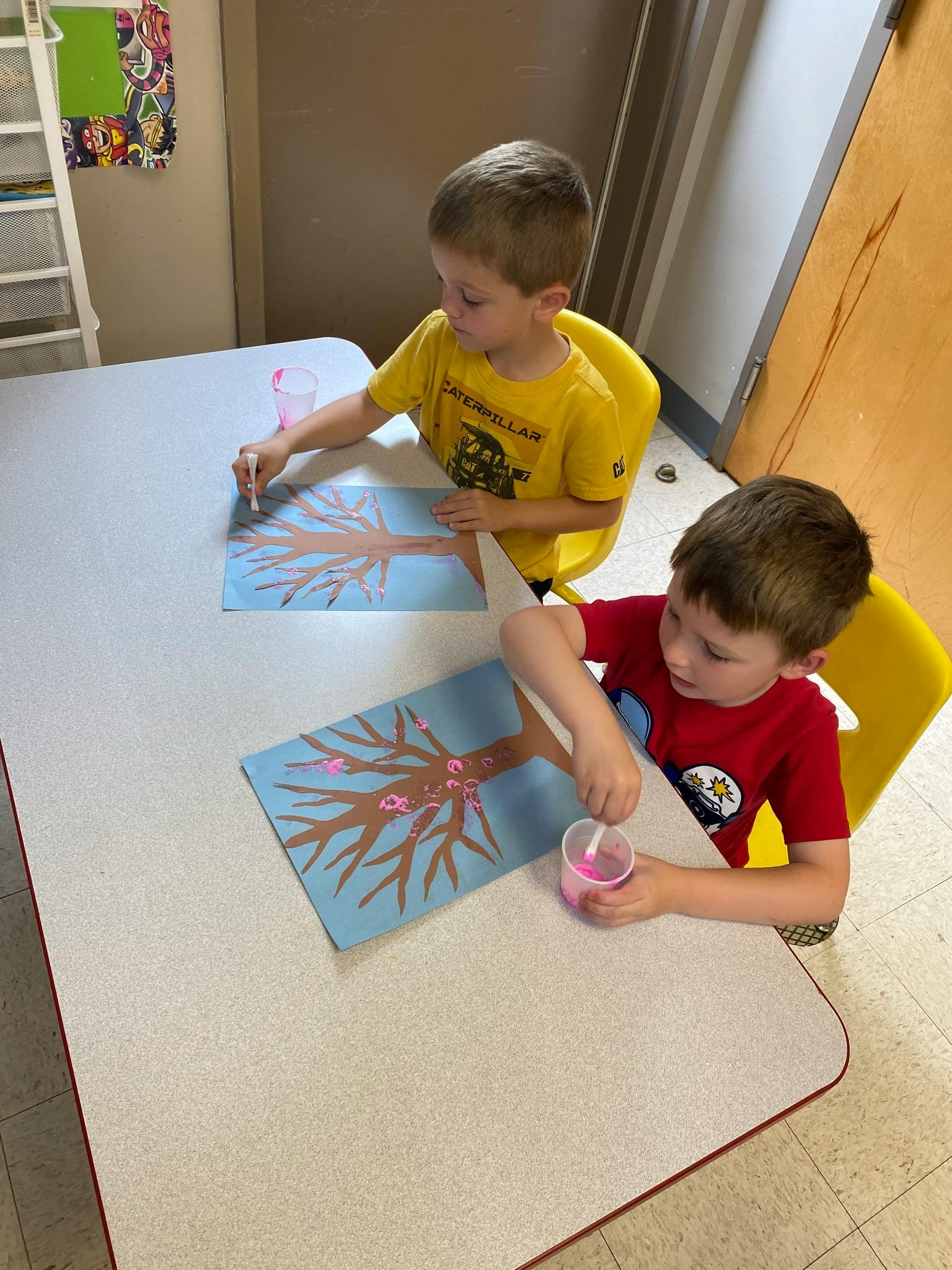 Two children painting tree pictures at a table