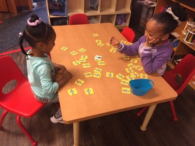 Two children sitting at a table with yellow cards spread out cards