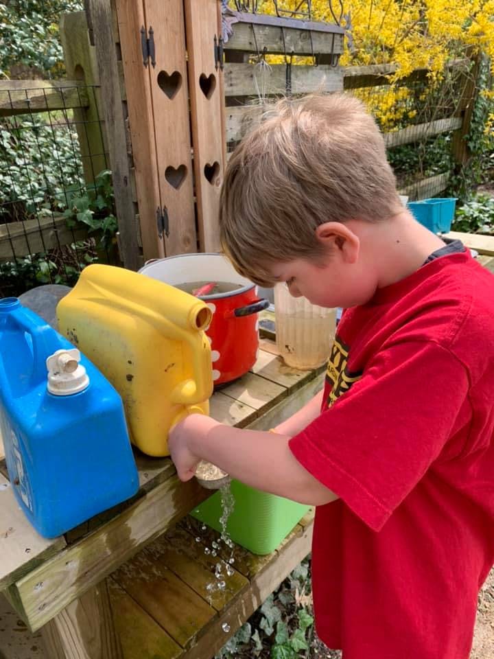 Child pouring water from a yellow container into a green bucket