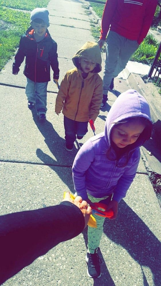 Person holding a child's hand, with two other children walking ahead on a sidewalk