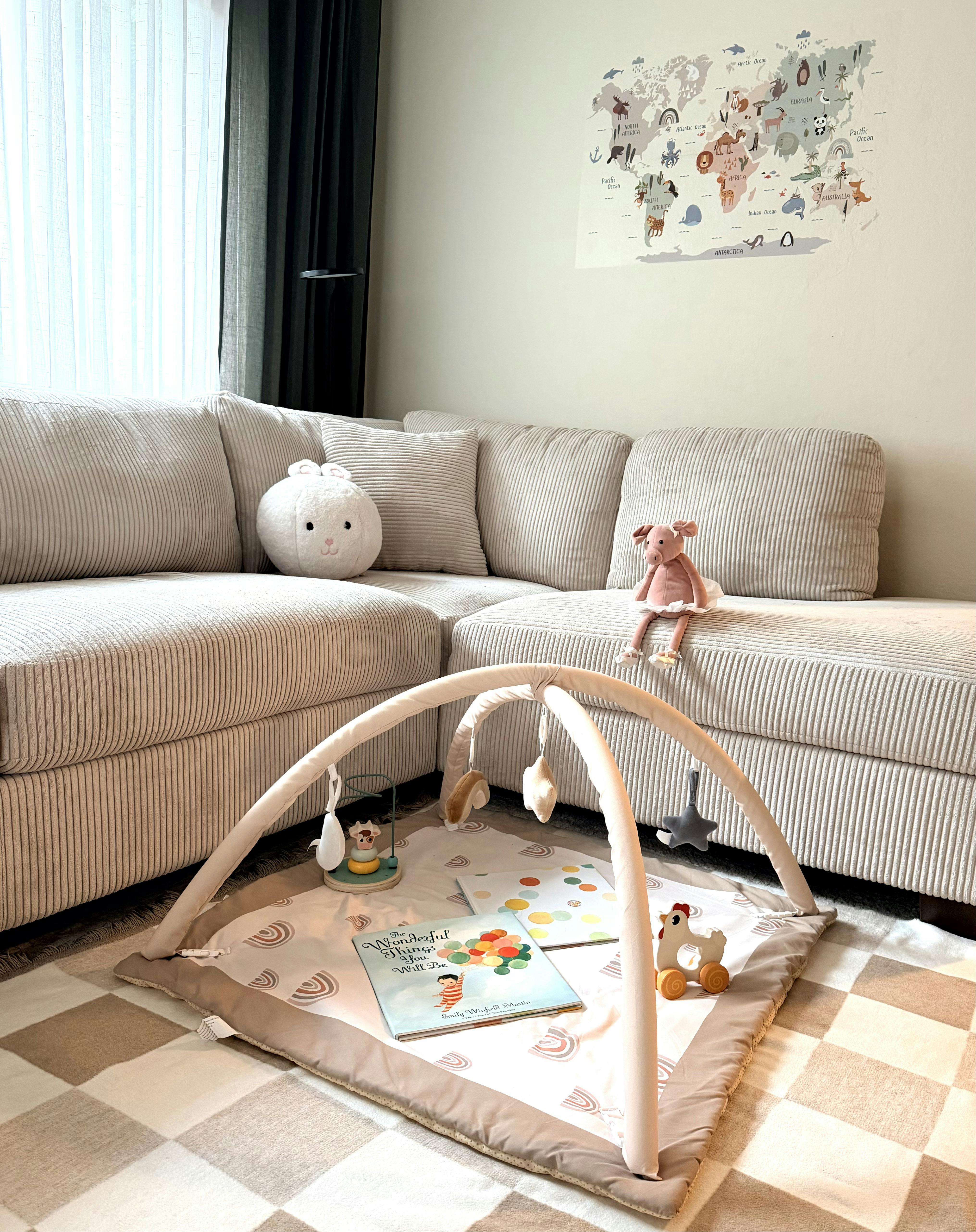 Baby play mat with books and toys on a rug next to a sofa with stuffed animals